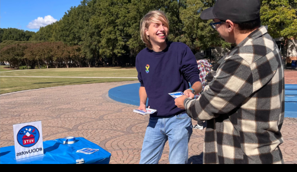 A student hands out a flyer to another student on ODU's campus.